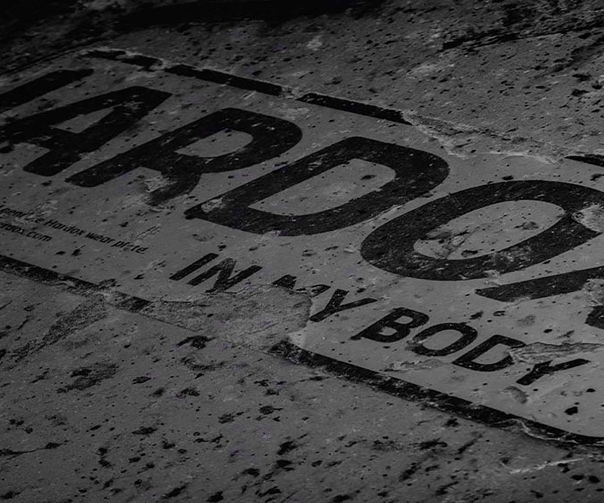 Black and white image of a Hardox In My Body sign that has seen rough use.